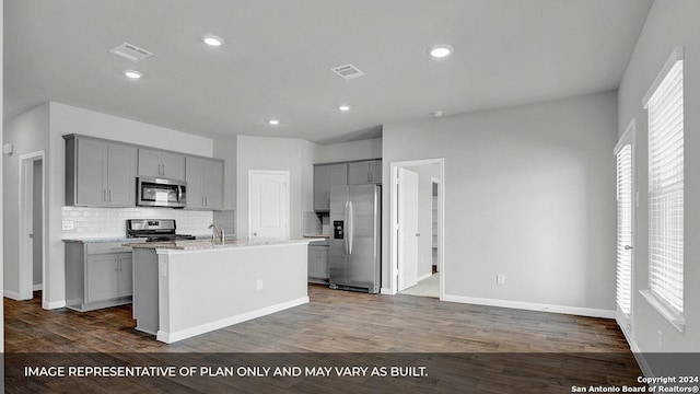 kitchen featuring stainless steel appliances, tasteful backsplash, dark hardwood / wood-style flooring, an island with sink, and gray cabinets