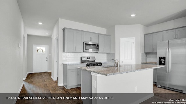 kitchen featuring sink, an island with sink, appliances with stainless steel finishes, tasteful backsplash, and dark hardwood / wood-style flooring