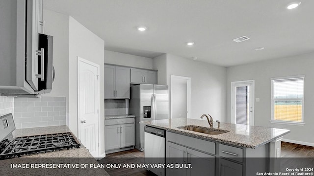 kitchen featuring sink, dark hardwood / wood-style floors, an island with sink, appliances with stainless steel finishes, and tasteful backsplash