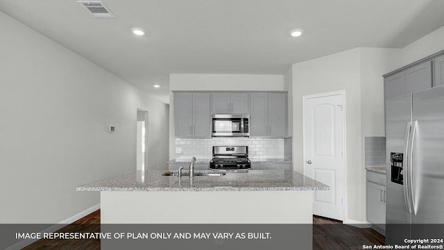 kitchen with a center island with sink, sink, dark hardwood / wood-style floors, light stone countertops, and stainless steel appliances