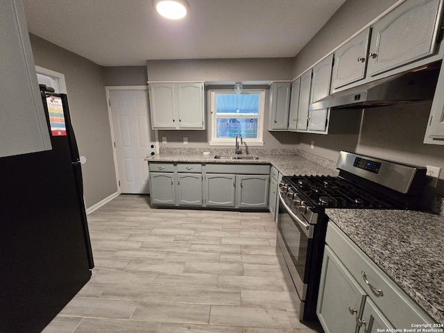 kitchen with stainless steel gas range oven, black refrigerator, sink, light hardwood / wood-style flooring, and gray cabinets