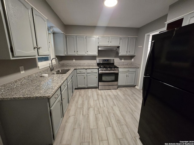 kitchen with stainless steel gas stove, sink, black fridge, gray cabinets, and light wood-type flooring