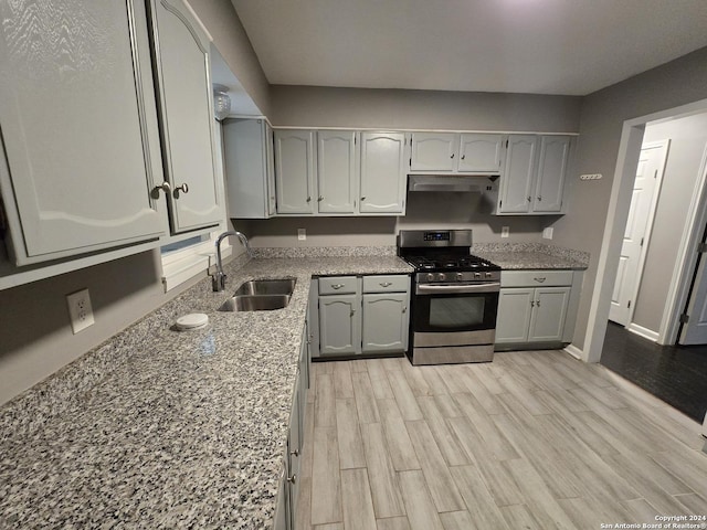 kitchen featuring gas stove, light stone counters, light hardwood / wood-style floors, and sink