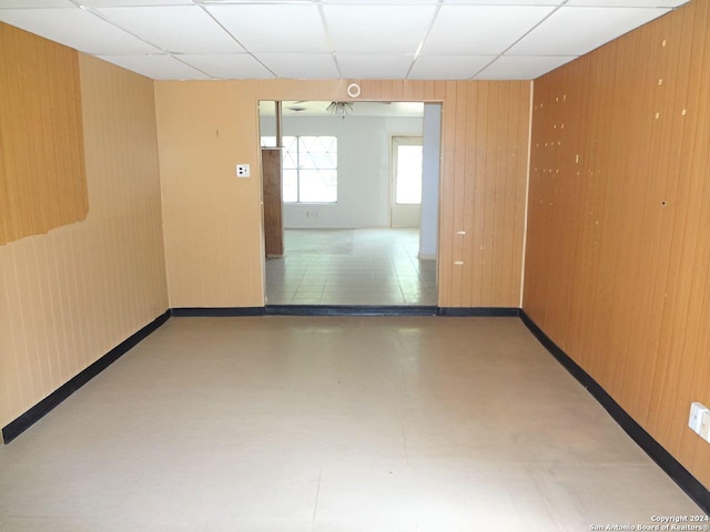 empty room featuring a drop ceiling and wood walls