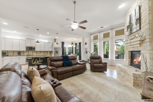 living room featuring light tile patterned floors, ceiling fan with notable chandelier, and a stone fireplace