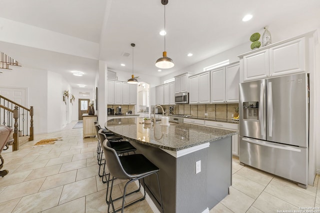 kitchen featuring tasteful backsplash, dark stone countertops, a kitchen island with sink, white cabinets, and appliances with stainless steel finishes