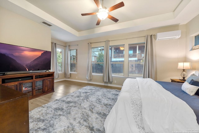 bedroom with a raised ceiling, ceiling fan, a wall mounted air conditioner, and hardwood / wood-style flooring