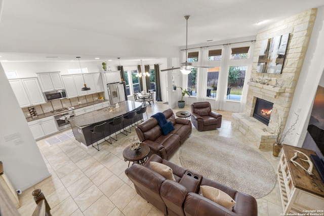 living room with ceiling fan with notable chandelier, a fireplace, light tile patterned floors, and vaulted ceiling