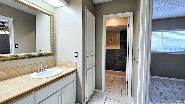 bathroom with tile patterned flooring, a textured ceiling, vanity, and tiled shower