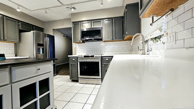 kitchen featuring backsplash, rail lighting, gray cabinetry, stainless steel appliances, and light tile patterned floors