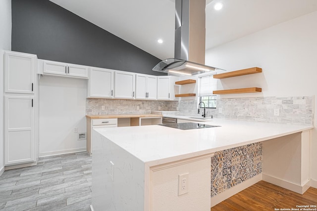 kitchen with kitchen peninsula, light wood-type flooring, island range hood, stovetop, and white cabinets