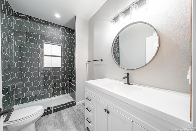 bathroom with tiled shower, hardwood / wood-style floors, vanity, and toilet