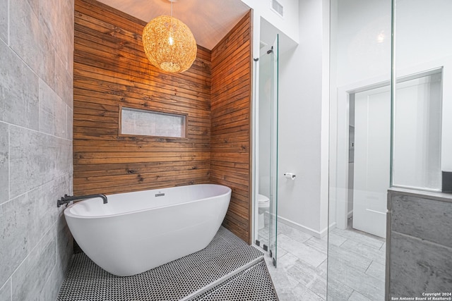 bathroom with a tub, wood walls, tile walls, and toilet