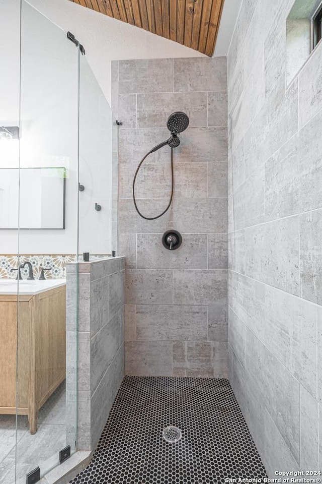 bathroom with a tile shower, vanity, and vaulted ceiling