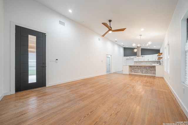 unfurnished living room featuring ceiling fan with notable chandelier, light wood-type flooring, and high vaulted ceiling