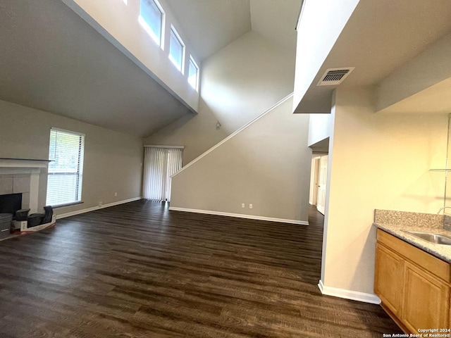 unfurnished living room with dark hardwood / wood-style flooring, high vaulted ceiling, a tiled fireplace, and sink