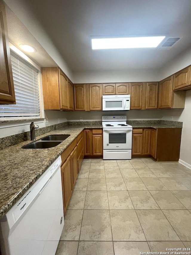 kitchen with light tile patterned floors, white appliances, sink, and dark stone counters