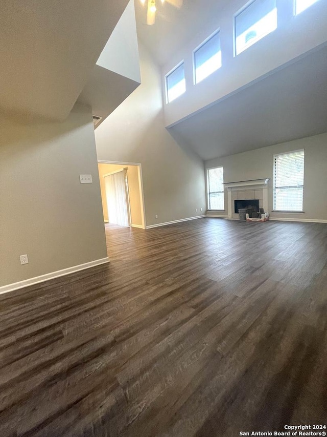 unfurnished living room featuring a tile fireplace, high vaulted ceiling, ceiling fan, and dark wood-type flooring