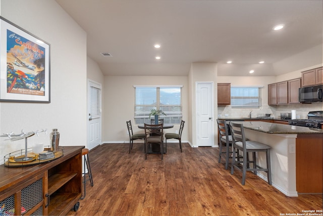 kitchen featuring a kitchen bar, backsplash, black appliances, dark stone countertops, and dark hardwood / wood-style floors