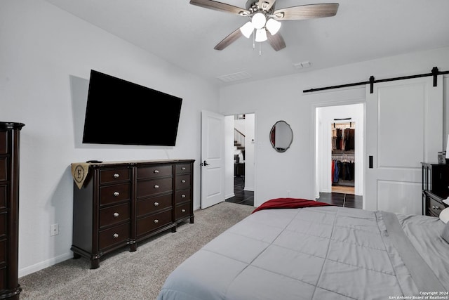 carpeted bedroom with a barn door, ensuite bathroom, and ceiling fan