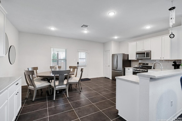 kitchen with white cabinets, dark tile patterned floors, tasteful backsplash, decorative light fixtures, and stainless steel appliances