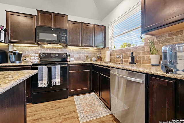 kitchen with light wood-type flooring, backsplash, light stone counters, dark brown cabinets, and black appliances