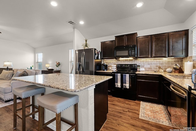 kitchen with a kitchen breakfast bar, black appliances, vaulted ceiling, and light hardwood / wood-style floors