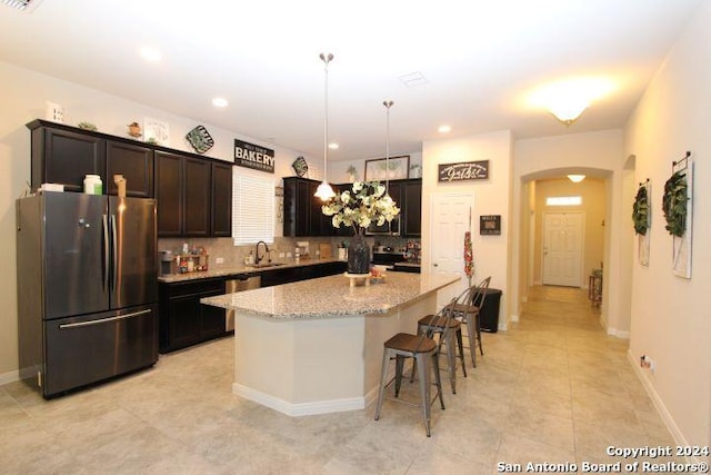 kitchen featuring light stone countertops, sink, pendant lighting, a kitchen island, and appliances with stainless steel finishes