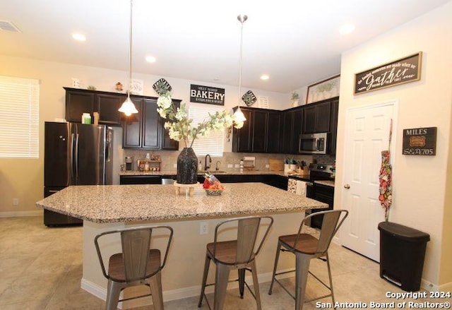 kitchen with pendant lighting, decorative backsplash, light stone countertops, appliances with stainless steel finishes, and a kitchen island