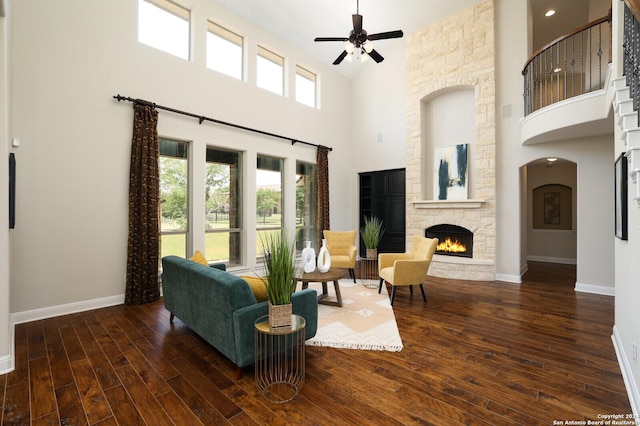 living room featuring ceiling fan, a stone fireplace, a towering ceiling, and dark wood-type flooring