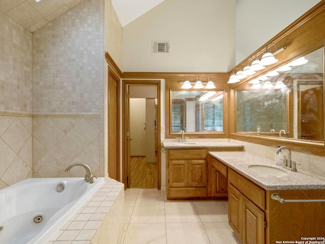 bathroom with tile patterned floors, vanity, tiled tub, high vaulted ceiling, and tile walls