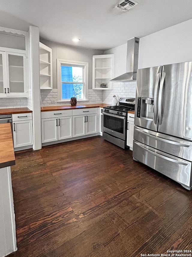 kitchen featuring dark hardwood / wood-style flooring, stainless steel appliances, wall chimney range hood, white cabinets, and butcher block countertops