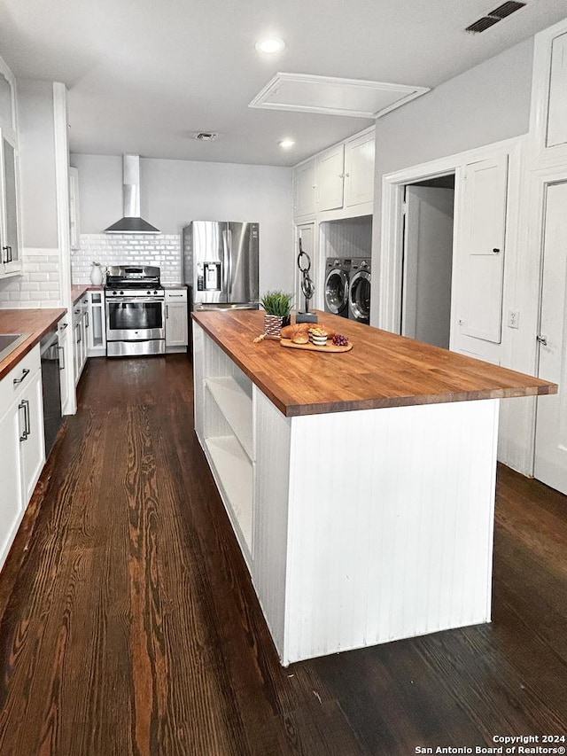 kitchen with stainless steel appliances, washer and clothes dryer, wall chimney range hood, a center island, and butcher block countertops