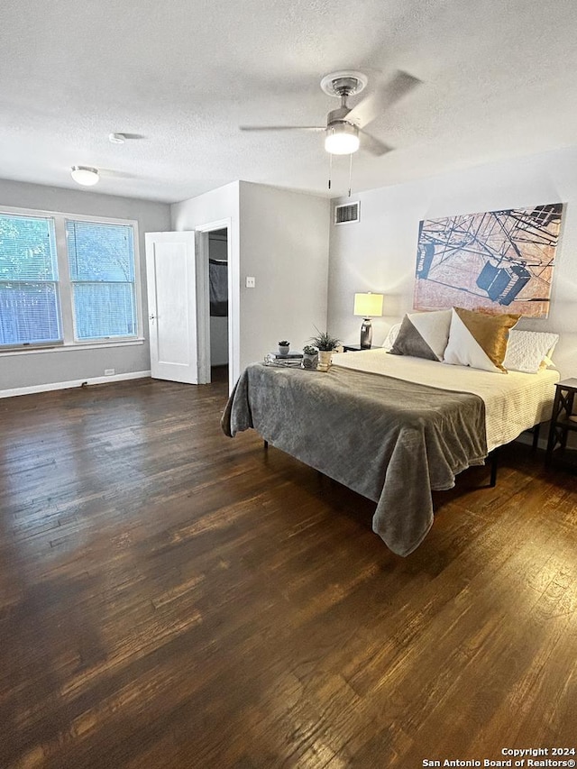 bedroom with a textured ceiling, ceiling fan, and dark wood-type flooring