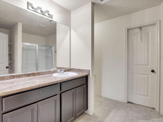 bathroom with tile patterned floors, vanity, an enclosed shower, and a textured ceiling