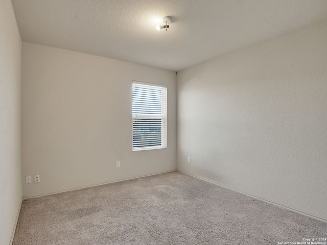 empty room with light colored carpet and a textured ceiling