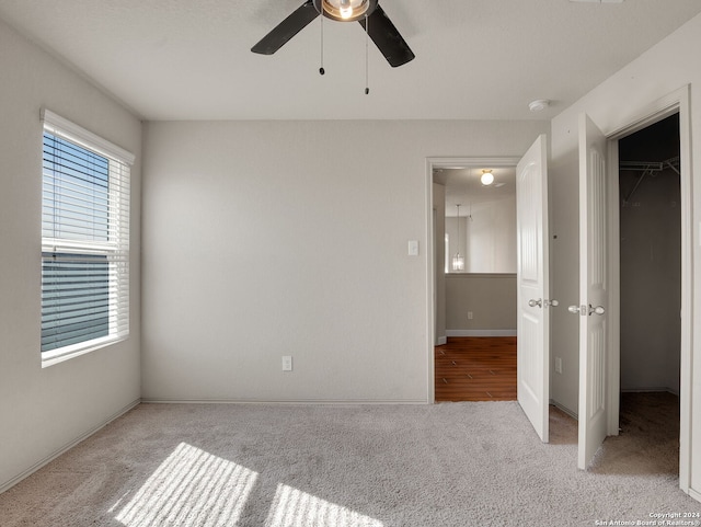 unfurnished bedroom with a walk in closet, ceiling fan, a closet, and light colored carpet