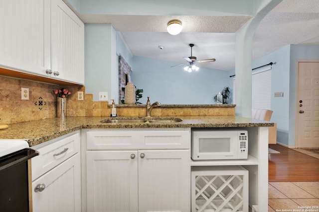 kitchen with kitchen peninsula, white cabinets, light stone counters, and sink