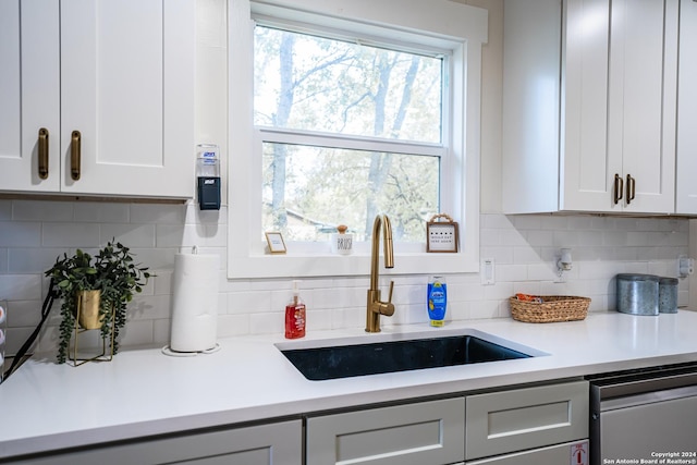 kitchen with tasteful backsplash, dishwashing machine, sink, and white cabinets