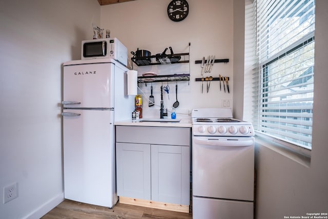 kitchen with light wood-type flooring, white appliances, white cabinets, and sink