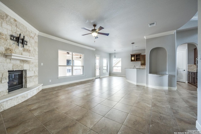 unfurnished living room with a stone fireplace, a textured ceiling, ceiling fan, tile patterned floors, and ornamental molding