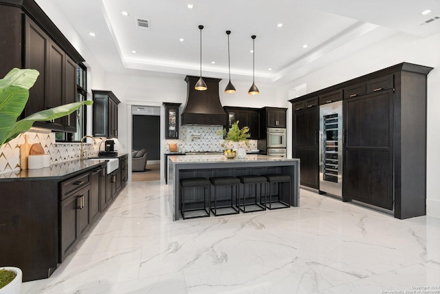 kitchen featuring a center island, sink, hanging light fixtures, a tray ceiling, and custom range hood