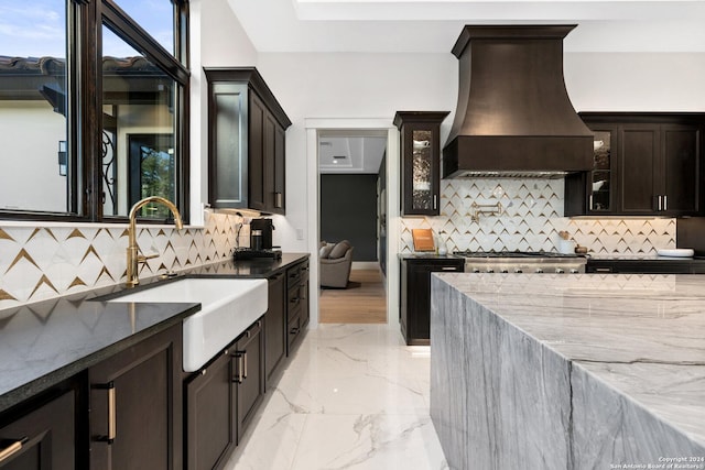 kitchen with premium range hood, dark stone countertops, sink, and backsplash