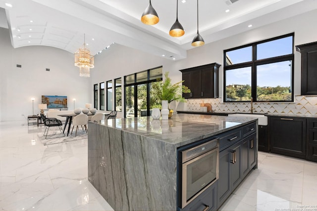 kitchen featuring oven, hanging light fixtures, dark stone countertops, tasteful backsplash, and a large island