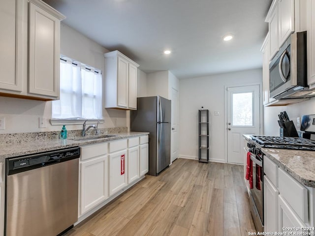 kitchen featuring light stone countertops, sink, light hardwood / wood-style floors, white cabinets, and appliances with stainless steel finishes