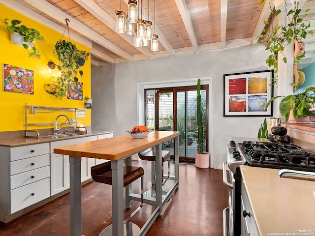 kitchen with beam ceiling, white cabinetry, stainless steel range with gas cooktop, pendant lighting, and wood ceiling