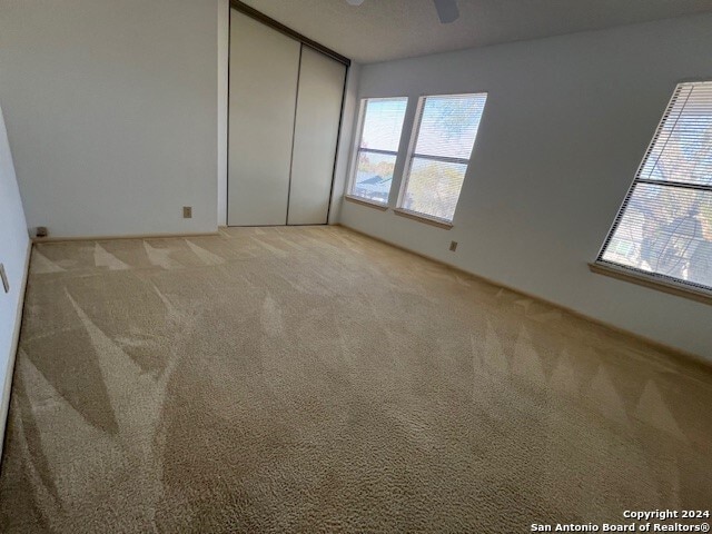 unfurnished bedroom with multiple windows, ceiling fan, a closet, and light colored carpet