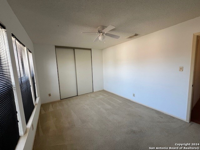 unfurnished bedroom with ceiling fan, a closet, light carpet, and a textured ceiling