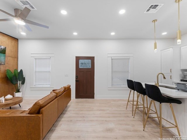 kitchen featuring a kitchen breakfast bar, ceiling fan, white cabinets, light hardwood / wood-style floors, and hanging light fixtures