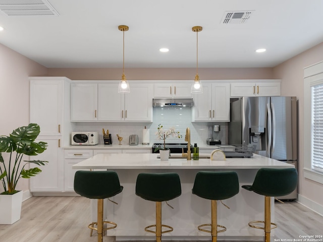 kitchen with pendant lighting, backsplash, white cabinets, light hardwood / wood-style floors, and stainless steel appliances